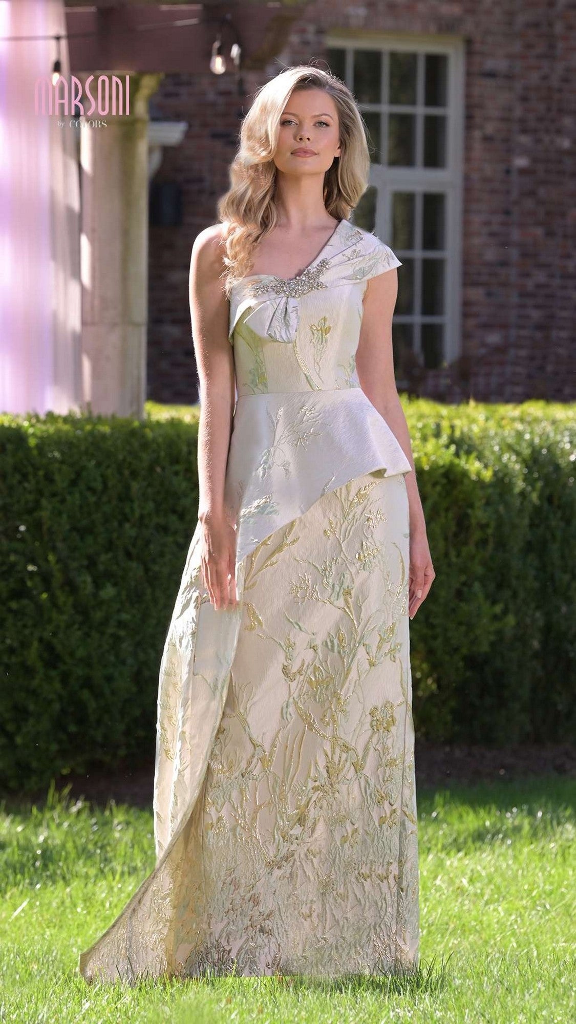A woman stands outside in the Marsoni MV1300 long formal dress, featuring a decorative neckline, cap sleeves, and elegant light-colored embroidery.